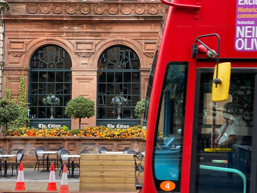 A vibrant city street featuring a historic building facade and a classic red bus in Glasgow, Scotland.
