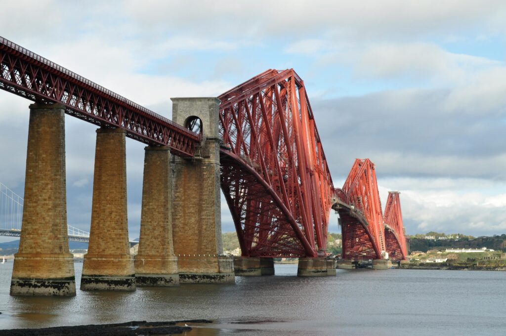 The famous red Forth Bridge stretching across the river under a cloudy sky.
