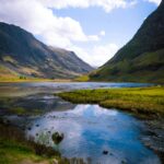 Breathtaking view of the Glencoe valley with a reflective lake in the Scottish Highlands under a sunny sky. Loch Achtriochtan Glencoe, whiste house glencoe
