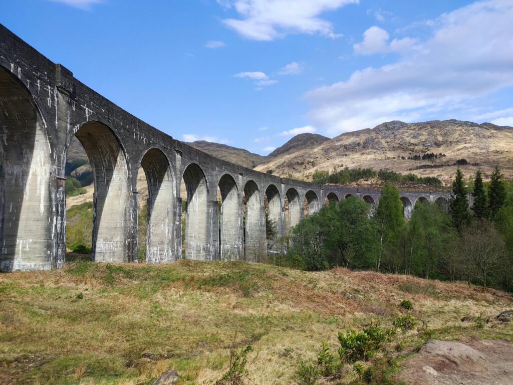 Scenic view of Glenfinnan Viaduct in Scotland with lush greenery and mountains.